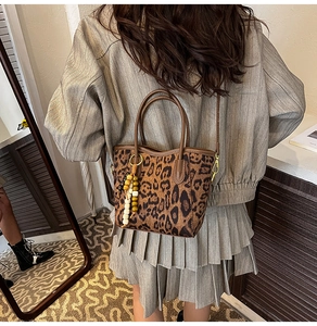 Détail du sac seau à imprimé léopard avec anses en cuir marron et breloque en perles