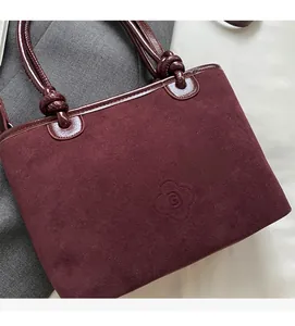 Close-up of burgundy suede tote bag with glossy leather trim and embossed flower logo