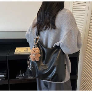 Detail of black pleated tote bag featuring brand logo and a brown plush bear charm