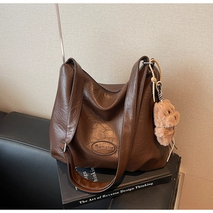 Detail of vintage pleated dark brown tote bag with cute plush bear charm on black books