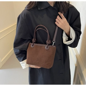Detailed close-up of brown suede bucket bag featuring embossed floral logo and leather handles