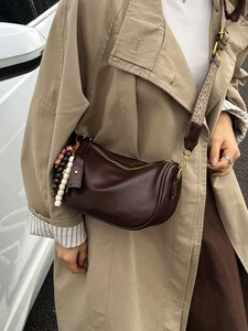 Deep brown leather Boston bag with retro woven strap and bead charms in a street setting