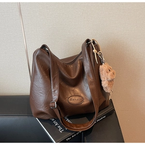 Detail of a brown pleated tote with vintage leather texture and a cute bear charm