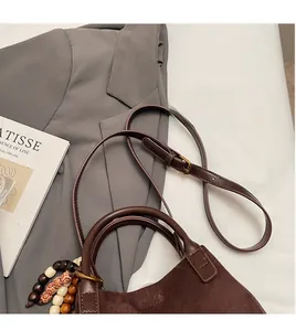 Detail der dunkelbraunen Wildledertasche mit Lederriemen und bunten Perlenquasten