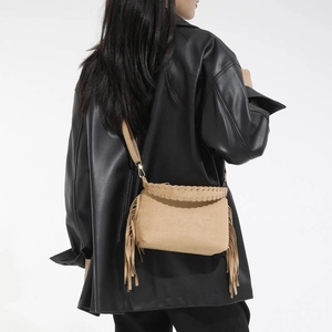 Detail view of khaki suede crossbody bag with long side fringes and woven edges on model