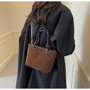 Macro detail of dark brown suede bucket bag featuring embossed logo and dual round handles