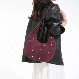 Dettaglio della borsa hobo in pelle scamosciata bordeaux con borchie dorate su modella