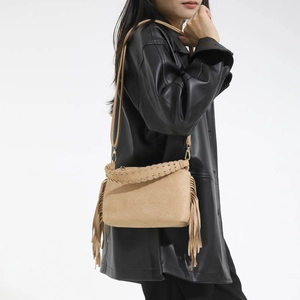 Detail of bohemian khaki suede crossbody bag with tassels and woven handle on a model