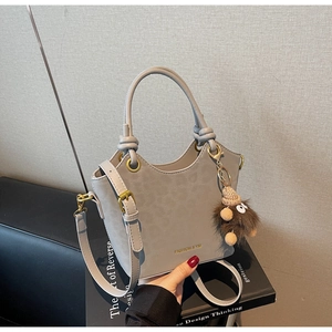 Dettaglio della borsa grigia minimalista con logo dorato e charm a forma di mostro