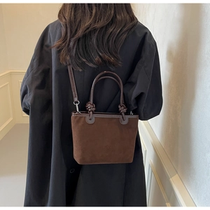 Detail of a brown suede bucket bag with leather handles and knotted strap detail
