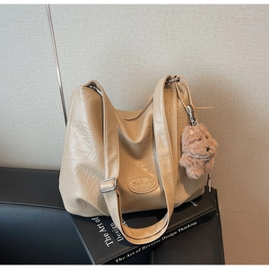Detail of beige hobo bag leather texture with Banatu logo and teddy bear charm accessory