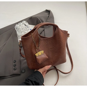 Détail du sac seau rétro en cuir PU marron avec mini accessoire et chaîne dorée élégante
