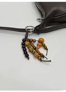 Dettaglio di ciondolo in perline di legno vintage su borsa a tracolla in pelle marrone