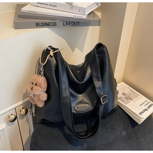 Detail of black textured tote bag with letter embossing and cute brown bear charm