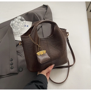 Détail d'un sac seau marron foncé avec chaîne dorée et mini pochette décorative assortie