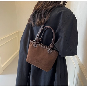 Detail view of a brown suede bucket bag with floral logo on a minimalist background