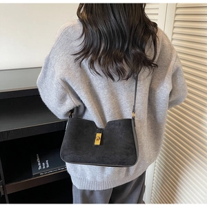 Détail du sac seau en daim noir avec fermoir doré porté par un mannequin au style épuré