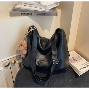 Detail of black textured hobo bag with Banatu logo and a brown plush teddy bear charm