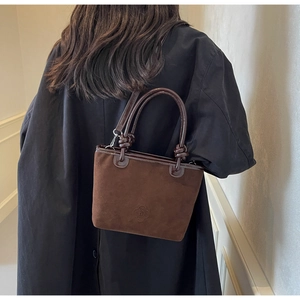 Detail of dark brown suede bucket bag featuring knotted handles and flower embossed logo