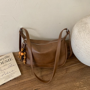 Brown vintage faux leather crescent shoulder bag with wooden bead tassel on wooden desk