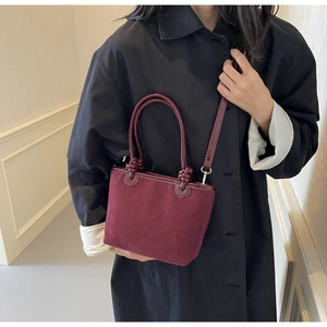 Detail of burgundy bucket bag with floral embossing, knot accents, and leather handles