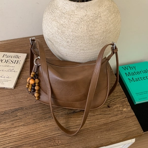 Detail view of brown matte leather shoulder bag with vintage beads charm on wooden table