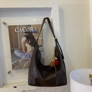 Detail view of large dark brown leather shoulder bag with decorative plush charms