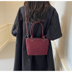 Detail view of burgundy leather bucket bag with knot handle on shoulder by model
