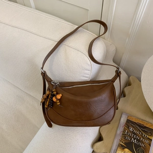 Detail of a brown leather crescent bag featuring a wooden bead and gourd tassel charm