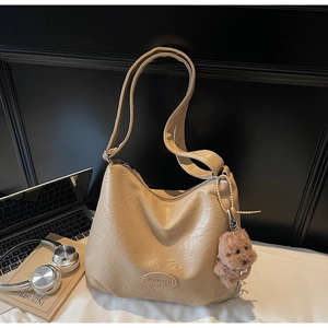Close-up of light brown pleated leather bag with Banatu logo and plush dog charm detail