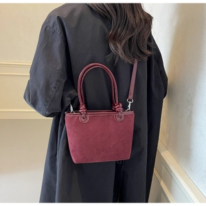 Detail of burgundy bucket bag featuring a unique knotted handle and embossed floral logo