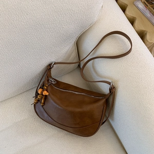 Brown leather hobo bag with wooden bead pendant on a beige sofa in home setting