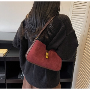 Détail du sac bandoulière en daim bordeaux avec fermoir doré porté par un mannequin
