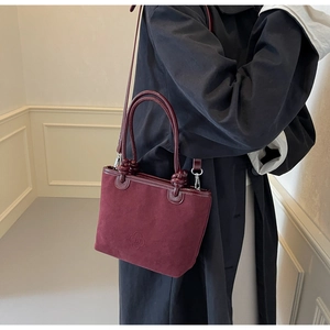 Macro view of burgundy suede bucket bag featuring embossed flower logo and smooth handle