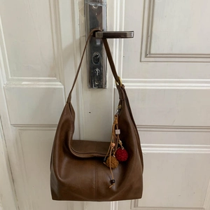 Detail view of brown faux leather hobo bag with ethnic tassel and wooden bead charm