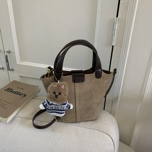 Detail of light tan suede bucket bag featuring a plush bear charm and brown leather handle