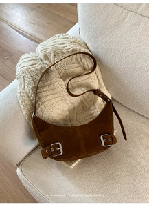 Detail of retro brown suede half-moon bag with silver buckles on a cozy knit sweater