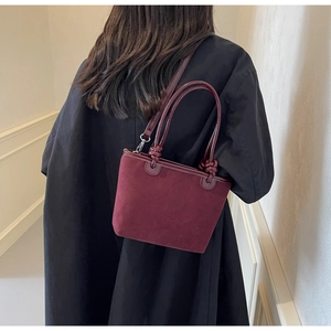 Detail view of burgundy suede bucket bag with knotted patent leather handles on model