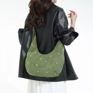 Borsa hobo in pelle scamosciata verde con borchie dorate indossata su giacca in pelle