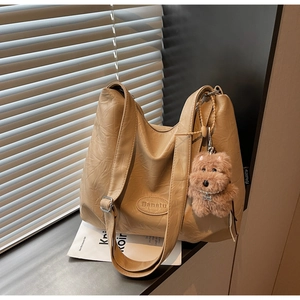 Detail of a pleated leather tote bag with a brand label and a cute puppy plush charm