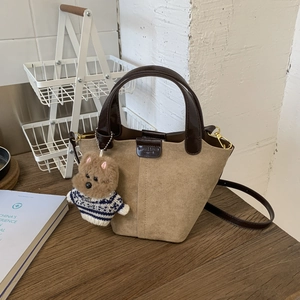 Detail of khaki suede bucket bag featuring leather trim and a cute teddy bear charm