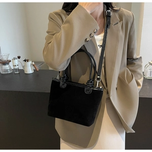 Detail of black suede bucket bag with knotted handle and leather trim on a model