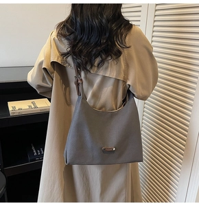 Detail of dark grey canvas hobo bag on model wearing khaki trench coat with leather strap