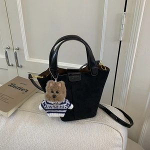 Detail of black suede and patent leather bucket bag with a cute plush dog pendant charm