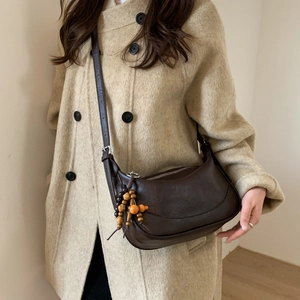 Detail of dark brown leather half-moon crossbody bag with vintage wooden bead charm