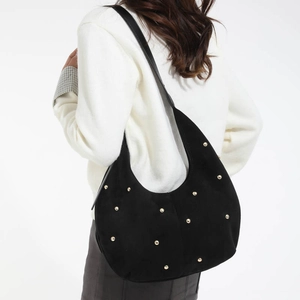 Dettaglio borsa hobo in camoscio nero con borchie dorate indossata sulla spalla