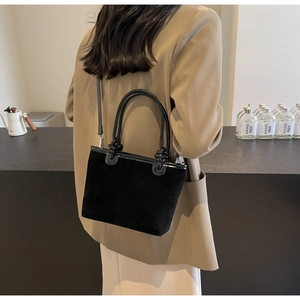 Detail of black suede bucket bag featuring embossed floral design and leather trim