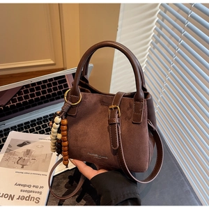 Nahaufnahme der braunen Wildleder-Beuteltasche mit Ledergriffen und Boho-Perlenanhänger