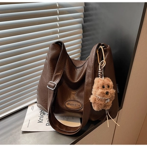 Detail of a large brown pleated leather tote bag with brand logo and plush charm