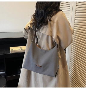 Grey canvas tote bag with leather straps worn by model in a stylish trench coat